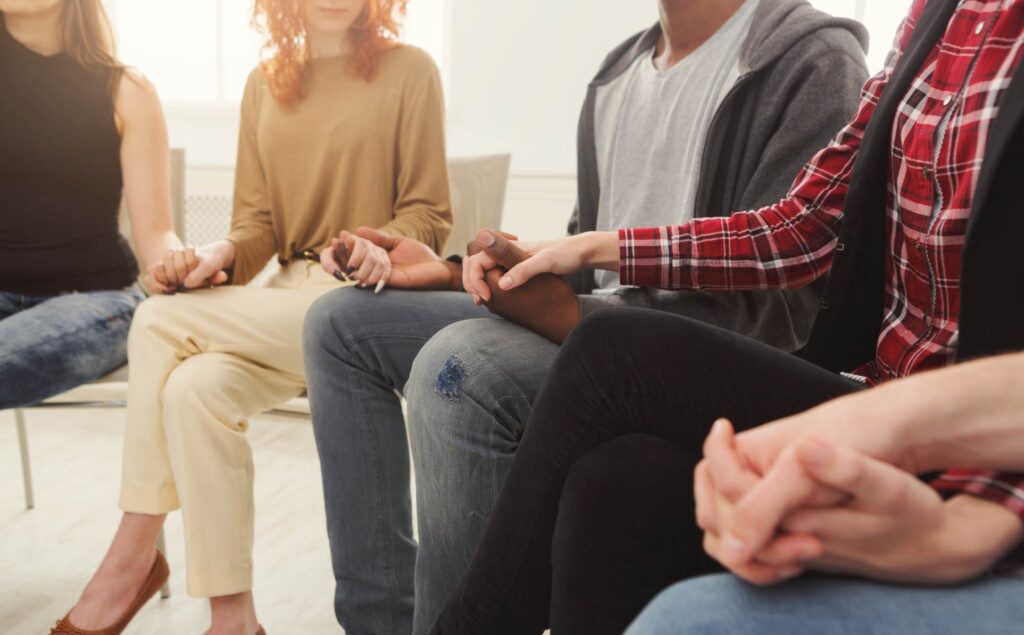 Circle of people holding hands during group therapy in Denver.