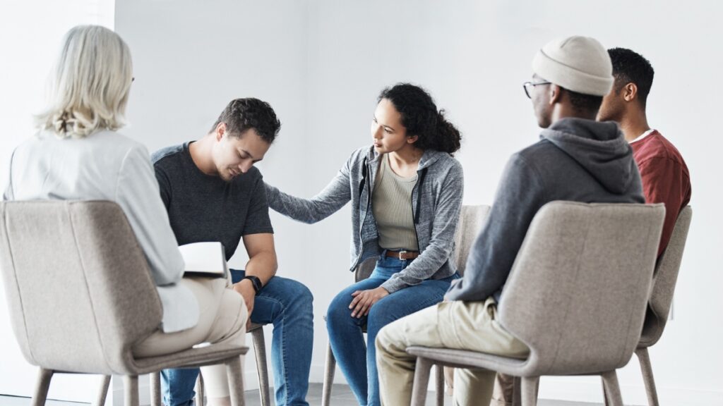 A man is comforted after sharing his story during a group therapy exercise.